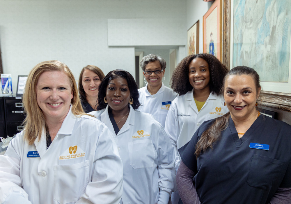 The image shows a group of individuals who appear to be healthcare professionals, possibly nurses or medical assistants, standing together in an office setting with a professional atmosphere.